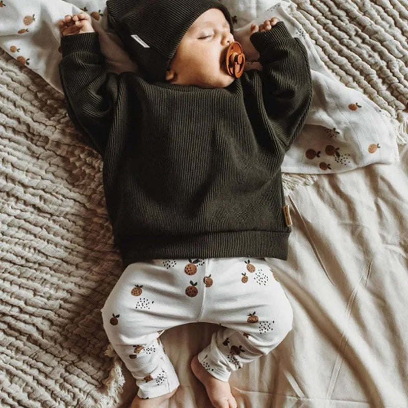Baby in donkergroene trui en biologische legging met herfstprint, liggend op bed met speen in