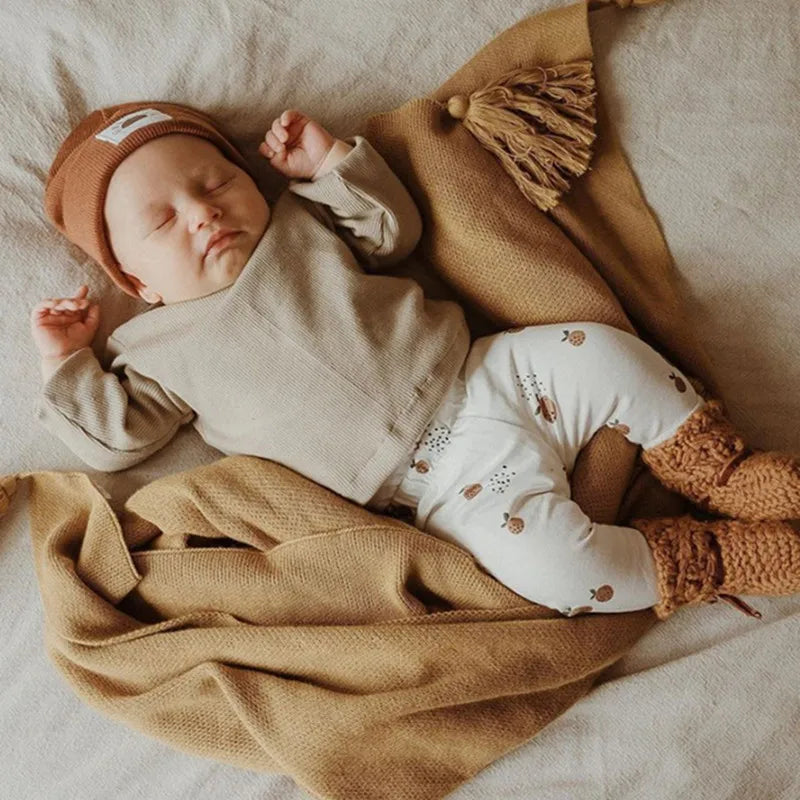 Slapende baby in beige outfit met biologisch katoenen legging met herfstachtige print, liggend op een zachte deken